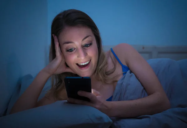 幸せな若い美しい女の子と話して彼女のスマート フォンを使用してインターネット上でサーフィンします 明るく楽しい女性ビデオ チャットで夜遅くリラックスし カジュアルな気分 携帯電話依存症の概念 — ストック写真