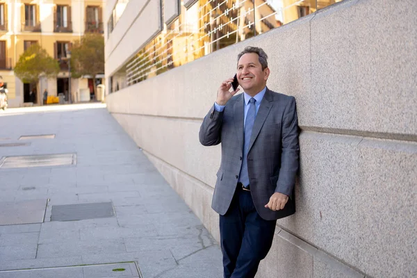 Портрет умного бизнесмена средних лет, гуляющего по городу и разговаривающего по мобильному телефону — стоковое фото