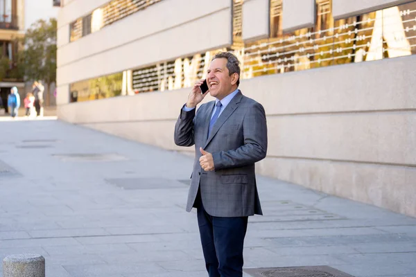Portrait of handsome middle aged smart businessman walking in the city talking on mobile phone — Stock Photo, Image