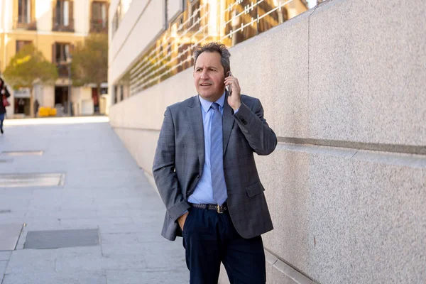 Portrait of handsome middle aged smart businessman walking in the city talking on mobile phone — Stock Photo, Image