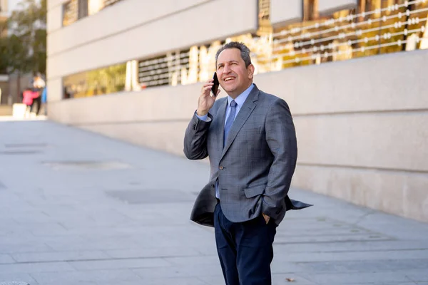 Portret van knappe middelste leeftijd slimme zakenman die lopen in de stad praten op mobiele telefoon — Stockfoto