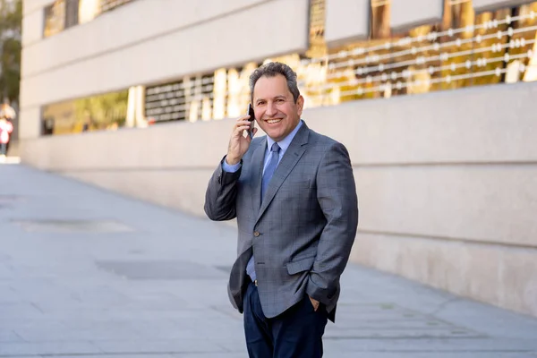 Portret van knappe middelste leeftijd slimme zakenman die lopen in de stad praten op mobiele telefoon — Stockfoto