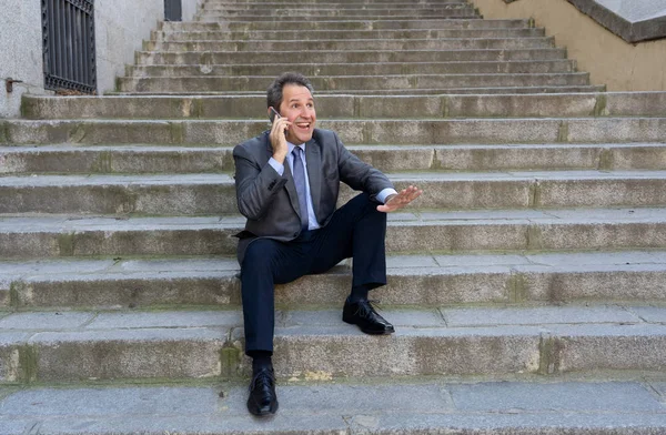 Happy mature business entrepreneur man sitting outdoors urban stairs working and using smart phone