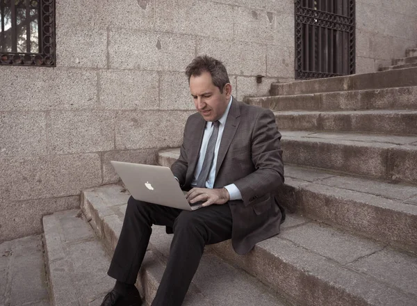 Happy mature business entrepreneur man sitting outdoors urban stairs working and using smart phone