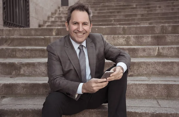 Happy mature business entrepreneur man sitting outdoors urban stairs working and using smart phone — Stock Photo, Image