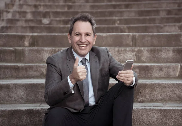 Счастливый зрелый бизнесмен-предприниматель сидит на открытом воздухе городских лестниц работает и с помощью смартфона — стоковое фото