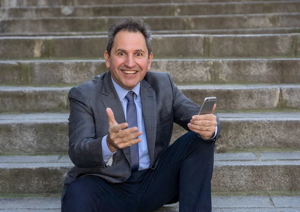 Щасливий зрілий бізнес-підприємець, який сидить на відкритому повітрі міські сходи, працюючи і використовуючи смартфон Стокове Зображення