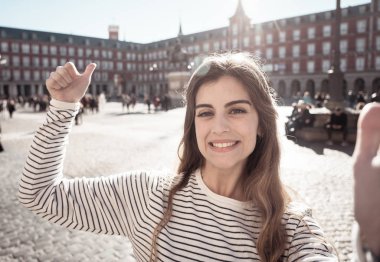Güzel genç öğrenci turist kadın mutlu ve heyecanlı Plaza Mayor Madrid içinde belgili tanımlık hareket eden tutan bir selfie alarak veya tablet. Neşeli yapım başparmak yukarıya hareket arıyorum. Turizm ve seyahat Avrupa'da.