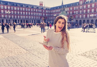Yol tariflerini bulma için güzel genç öğrenci turist kadın mutlu ve heyecanlı Plaza Mayor Madrid bakarak seyahat mobil uygulaması veya akıllı telefon kontrol. Turizm ve teknoloji bir Avrupa yolculuk.