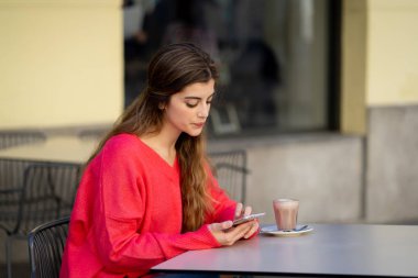 Neşeli bir kahve içme, ileti gönderme ve akıllı cep telefonu dışında bir şehir kahve dükkanında sohbet arayan genç ve güzel kadın. Mutlu ve neşeli hissediyorum. Yaşam tarzı ve teknoloji.