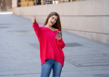 Kapısının önündeki tabelada yukarı şehir içinde Sokak yapma mobil akıllı telefon kullanan genç çekici mutlu kadın. Güzel genç şık kıyafetlerle tasasız hissediyor. Yaşam tarzı ve teknoloji kullanımı kavramı.