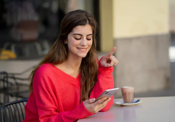 Pretty Happy young woman chatting and using smart mobile phone app looking cheerful drinking coffee in a urban coffee terrace. In online dating, mobile app, internet, connections and technology use.