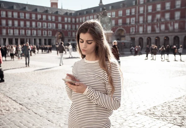 Lost young tourist woman checking smart mobile phone trying to find directions. Looking worried and thoughtful consulting the cellphone app. In tourism in Europe, Spain, Madrid and technology concept.