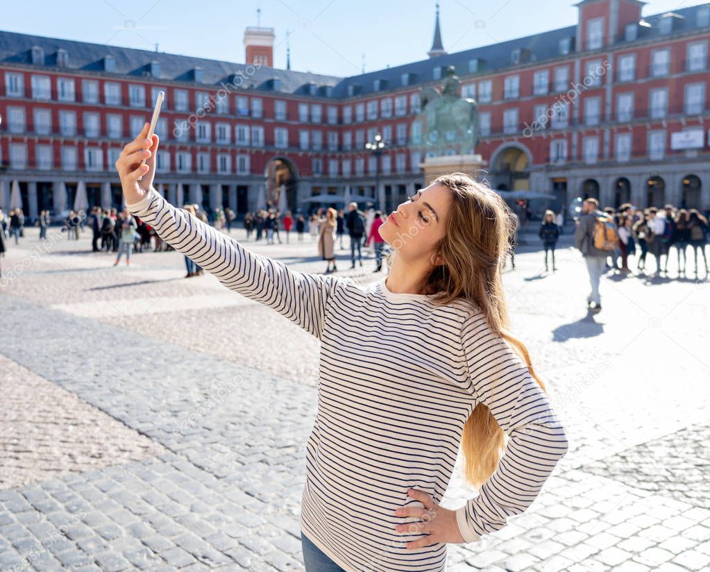 Beautiful young caucasian student tourist woman taking a selfie or video for her tourism and travel around the world blog web in Plaza Mayor Madrid Spain. In social media and vacations in europe.
