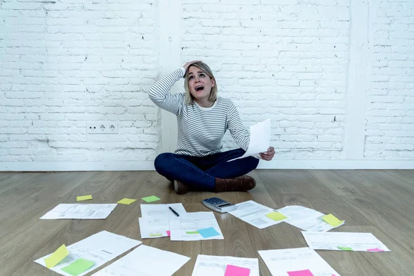 Portrait of worried young woman feeling stressed and desperate on the ground with calculator accounting expenses not able to pay mortgage. In paying debts and domestic bills and financial problems.