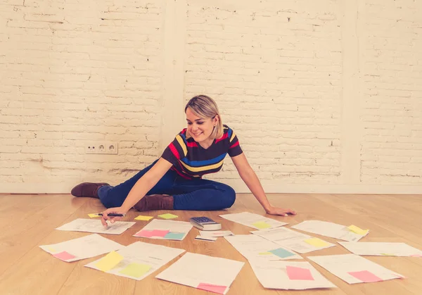 Happy entrepreneur woman on the floor surrounded by papers calculating budget and bills at new studio office. In small business owner, finances, mortgage and money financial planning concept.