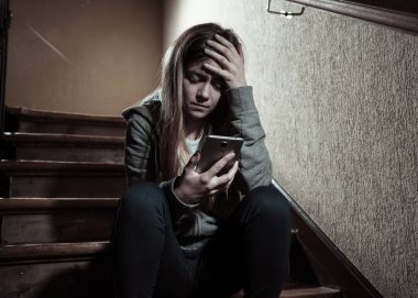 Siber zorbalık istismarı muzdarip online Stalker genç kız kurbanı yalnız ve umutsuz koyu ışık merdivenlerde oturan duygu. İnternet tehlikeleri, çevrimiçi bakım ve taciz konsepti.