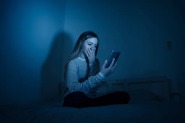 悲伤绝望的年轻少女在智能手机上遭受网络膨胀和骚扰 感觉孤独和绝望的晚上坐在床上 网络欺凌与网络概念的危害 — 图库照片