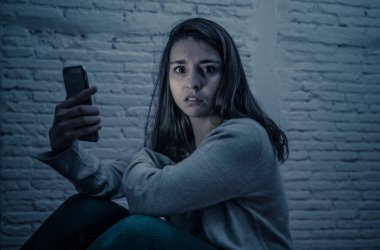 Gece katta üzgün korkmuş genç kadın portre vurguladı ve akıllı cep telefonu tehdit siber zorbalık taciz muzdarip. Stalker tarafından istismar online olmak umutsuz ve depresif.