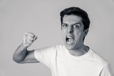 Siyah ve beyaz genç beyaz erkek yakın kadar öfkeli bir yüz. Öfkeli, deli, öfke içinde yumruklanmış yumruk ile agresif görünüyorsun. Beyaz arka planda izole edilmiştir. Yüz ifadeleri ve duygular.