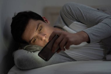 Addicted Man sohbet ve yatakta gece geç saatlere kadar akıllı telefon ile Internette sörf. Sıkılmış, uykusuz ve kasvetli ışık ile karanlık odada yorgun. Uykusuzluk ve mobil bağımlılık kavramı.