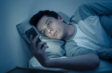 Addicted Man sohbet ve yatakta gece geç saatlere kadar akıllı telefon ile Internette sörf. Sıkılmış, uykusuz ve kasvetli ışık ile karanlık odada yorgun. Uykusuzluk ve mobil bağımlılık kavramı.