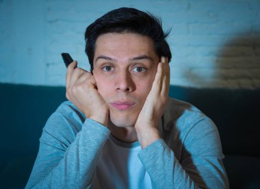 Genç bored adam kanepede oturan başka bir film veya gece geç saatlere kadar canlı spor için uzaktan kumanda zap kullanarak. İlgilenmiyor ve uykusuz görünüyorsun. İnsanlar, uykusuzluk, televizyon ve sedanter yaşam tarzı.