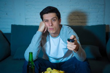 Gece geç saatlere kadar başka bir film veya canlı spor için TV uzaktan kumanda zap kullanarak kanepede genç sıkılmış adam. İlgi ve uykusuz bira içme bakıyor. İnsanlar, uykusuzluk ve sedanter yaşam tarzı.