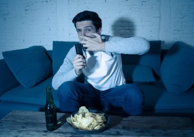 TV izlerken ve uzaktan kumanda tutarak korku, anksiyete jestleri yapma korkmuş ve şok hissi genç adam yaşam tarzı portre. Şiddet ve korku filmleri ve serisi internet akışı.