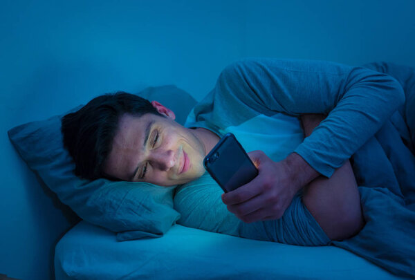 Молодой наркоман по ночам просыпается в постели, используя смартфон для чата, флирта и отправки текстовых сообщений. В области коммуникации, интернет-зависимости и злоупотребления социальными сетями
