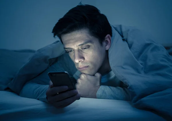 若い携帯電話の中毒男は チャット いちゃつくとテキストメッセージを送信するためのスマートフォンを使用して 夜にベッドで目を覚ます コミュニケーション インターネット中毒とソーシャルメディアネットワーク乱用の概念 — ストック写真