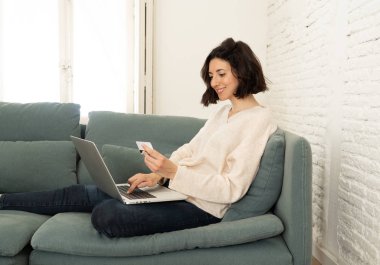 Evde dizüstü bilgisayar ve kredi kartı alışveriş online oturan mutlu genç kadın