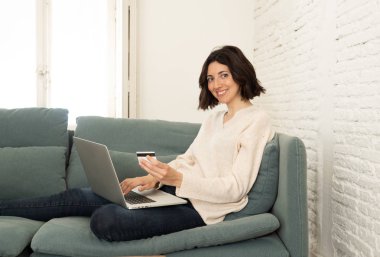 Evde dizüstü bilgisayar ve kredi kartı alışveriş online oturan mutlu genç kadın