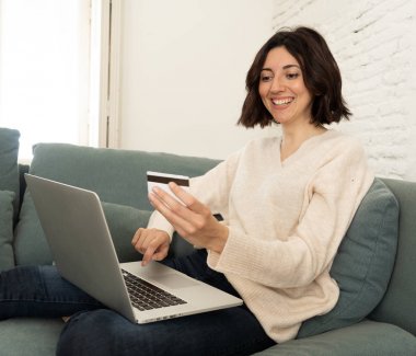 Evde dizüstü bilgisayar ve kredi kartı alışveriş online oturan mutlu genç kadın