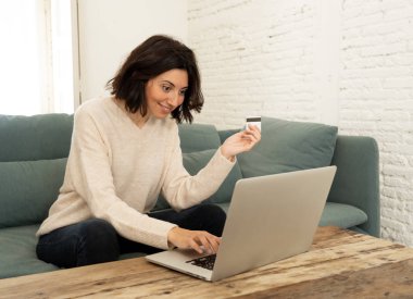 Evde dizüstü bilgisayar ve kredi kartı alışveriş online oturan mutlu genç kadın