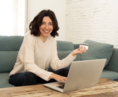 Evde dizüstü bilgisayar ve kredi kartı alışveriş online oturan mutlu genç kadın