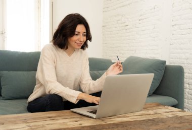 Evde dizüstü bilgisayar ve kredi kartı alışveriş online oturan mutlu genç kadın