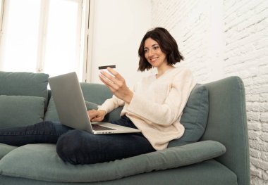 Evde dizüstü bilgisayar ve kredi kartı alışveriş online oturan mutlu genç kadın