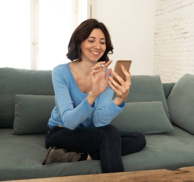 Mutlu genç kadın evde kanepede oturan onu akıllı telefon kullanarak. Boş zaman ve mobil bağımlılık