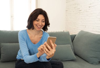 Mutlu genç kadın evde kanepede oturan onu akıllı telefon kullanarak. Boş zaman ve mobil bağımlılık