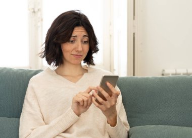 Mutlu genç kadın evde kanepede oturan onu akıllı telefon kullanarak. Boş zaman ve mobil bağımlılık