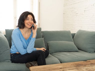 Mutlu genç kadın evde kanepede oturan akıllı telefonda konuşuyor. Eğlence ve teknolojide