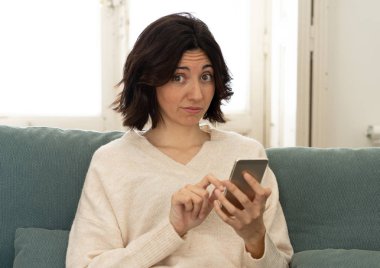 Mutlu genç kadın evde kanepede oturan onu akıllı telefon kullanarak. Boş zaman ve mobil bağımlılık