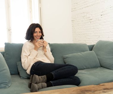 Sıcak kahve veya çikolata içen genç oldukça rahat kadın yaşam tarzı portre kanepede mutlu gülümseyerek evde mutlu ve rahat duygu. Boş zamanlarında, huzurlu yaşam, mutluluk yaşam tarzı kavramı.