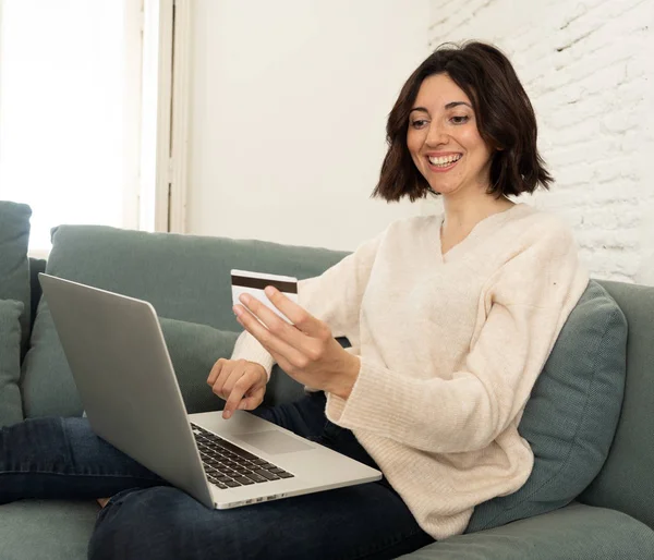 Joyeux jeune femme assise avec un ordinateur portable et une carte de crédit shopping en ligne à la maison — Photo