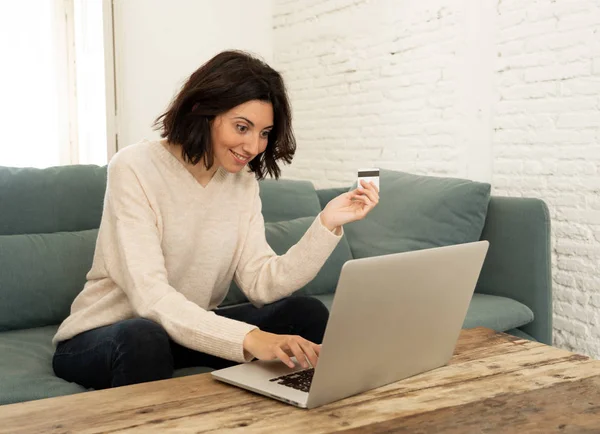 Evde dizüstü bilgisayar ve kredi kartı alışveriş online oturan mutlu genç kadın