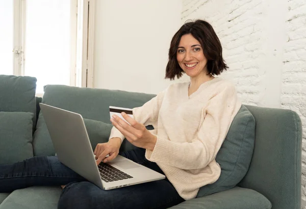 Joyeux jeune femme assise avec un ordinateur portable et une carte de crédit shopping en ligne à la maison — Photo