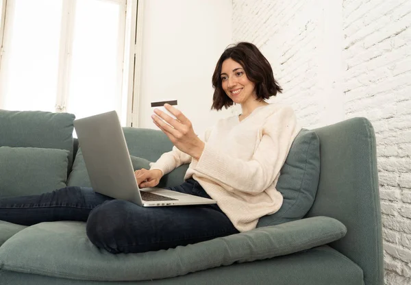 Joyeux jeune femme assise avec un ordinateur portable et une carte de crédit shopping en ligne à la maison — Photo