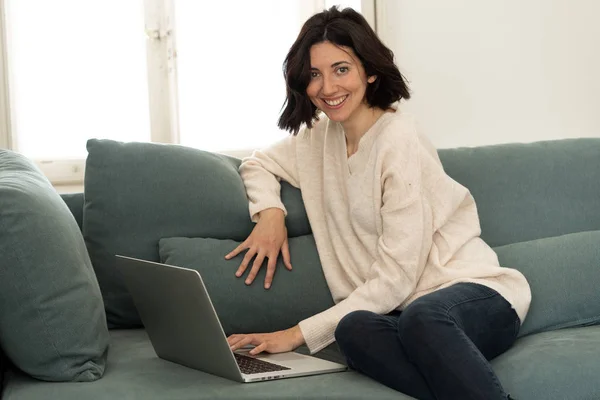 Donna felice che lavora su laptop navigando su internet e social media seduta sul divano di casa . — Foto Stock
