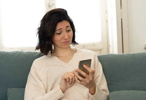 Happy young woman using her smart phone sitting on sofa at home. In leisure and mobile addiction — Stock Photo, Image